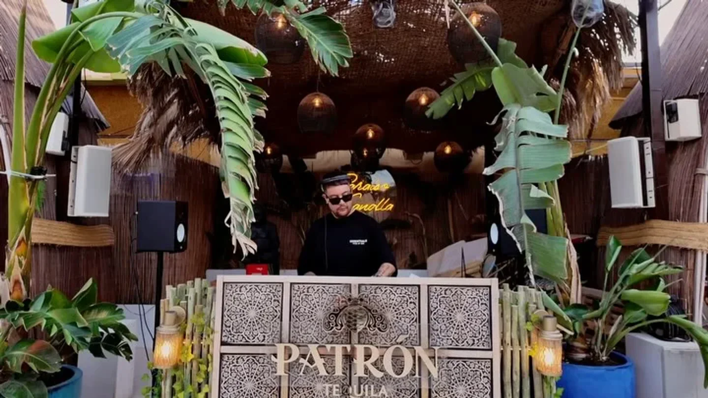 DJ at Baloo Ibiza spinning tunes amidst tropical decor and Patron Tequila branding.