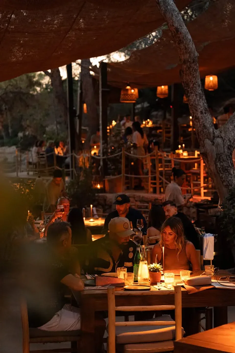 Romantic evening ambiance at Cala Gracioneta beach club in Ibiza with candlelit tables under woven lamps.