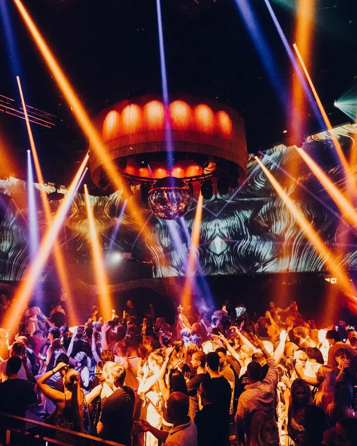 Energetic dance floor at Club Chinois in Ibiza, illuminated by vibrant lights and a disco ball.