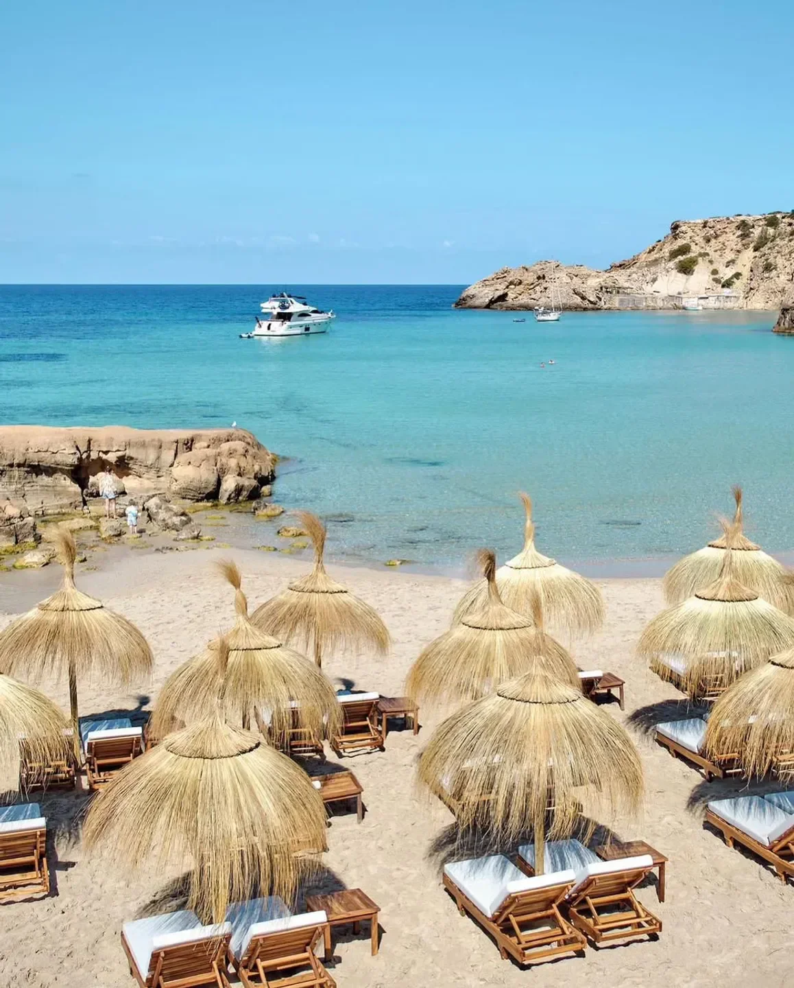 Beachfront scene at Cotton Beach Club in Ibiza, featuring beach umbrellas and crystal water