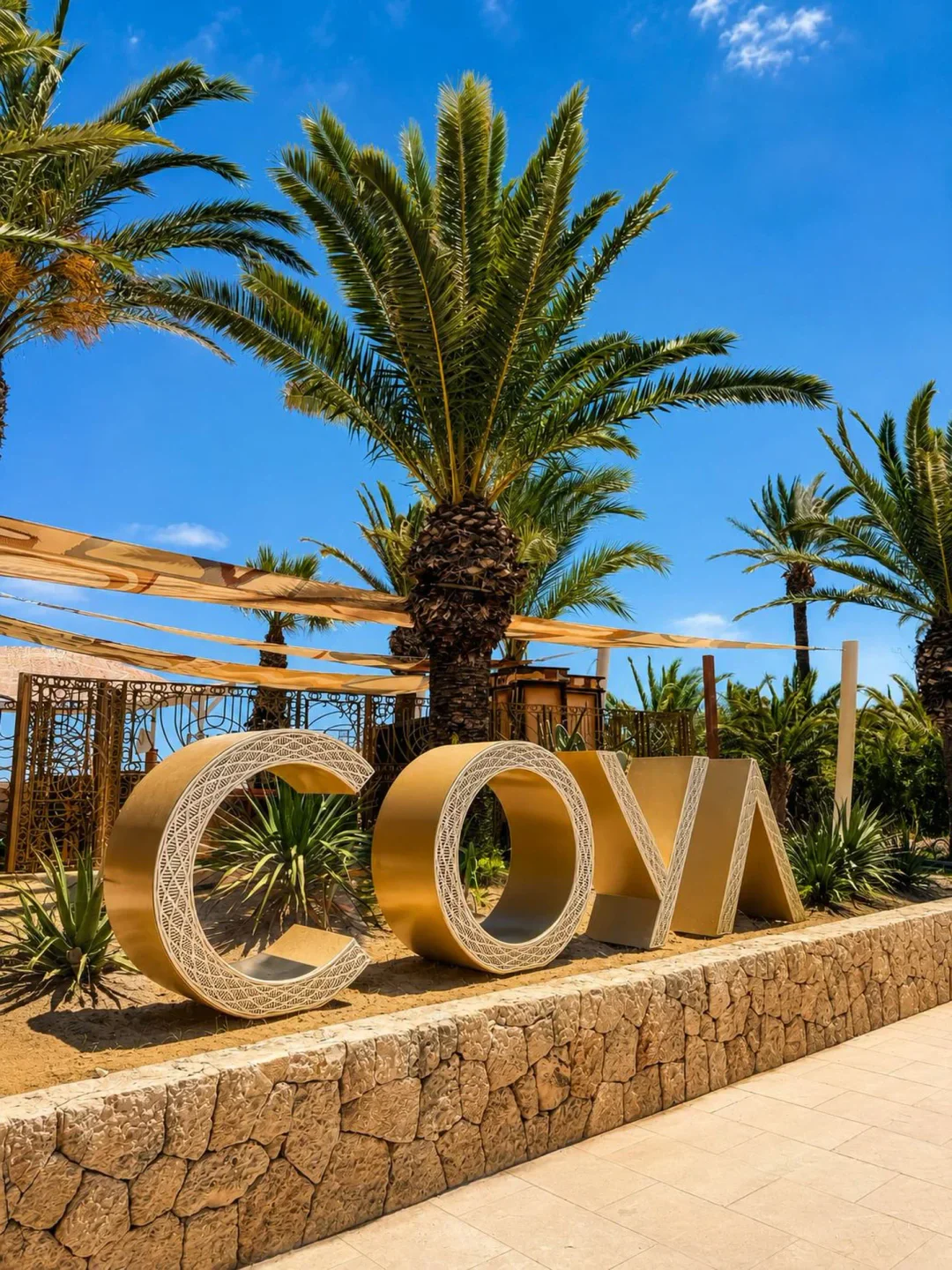 Golden "COYA" sign with palm trees at COYA Beach Ibiza, showcasing tropical vibes.