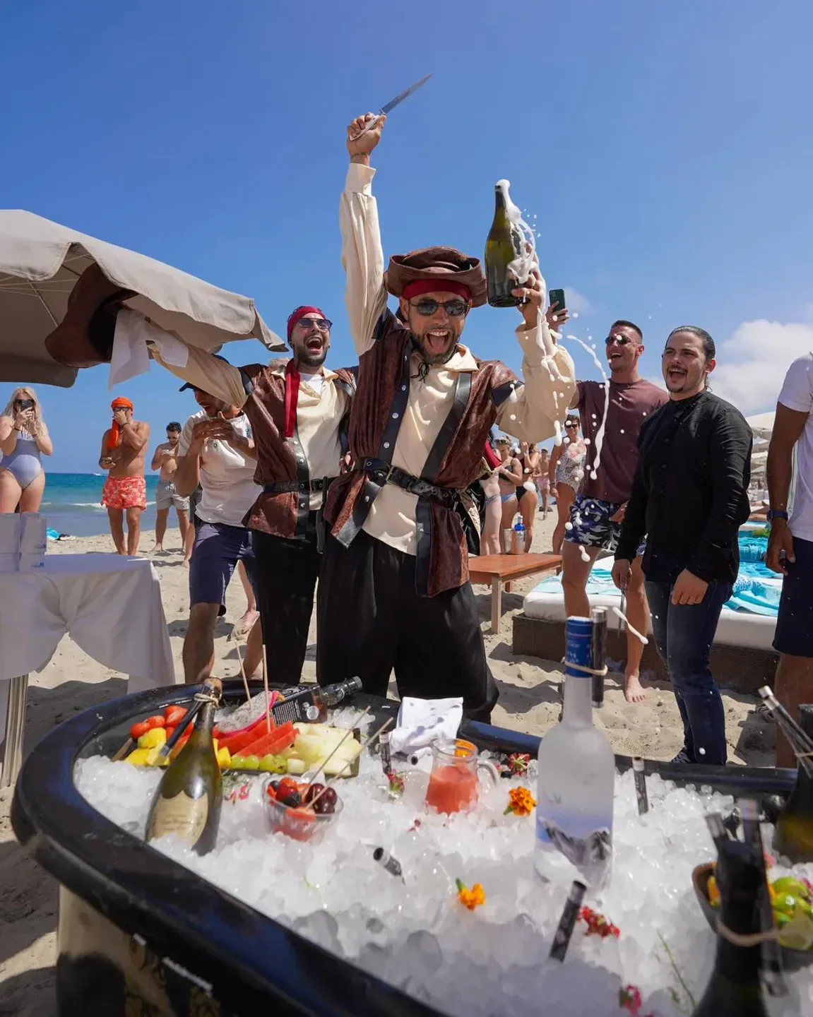 Celebratory champagne spray at Nassau Beach Club Ibiza with costumed performers on the beach.