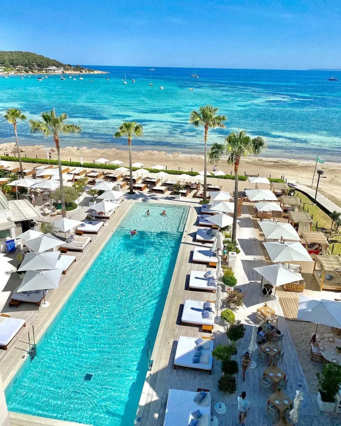 Nobu Ibiza beach club, crystal clear pool, white sunbeds, and turquoise sea view.