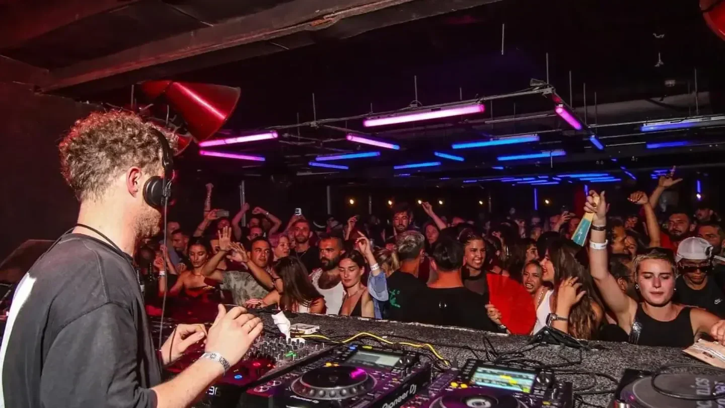DJ playing at Octan Ibiza nightclub, crowd dancing under colorful lights.