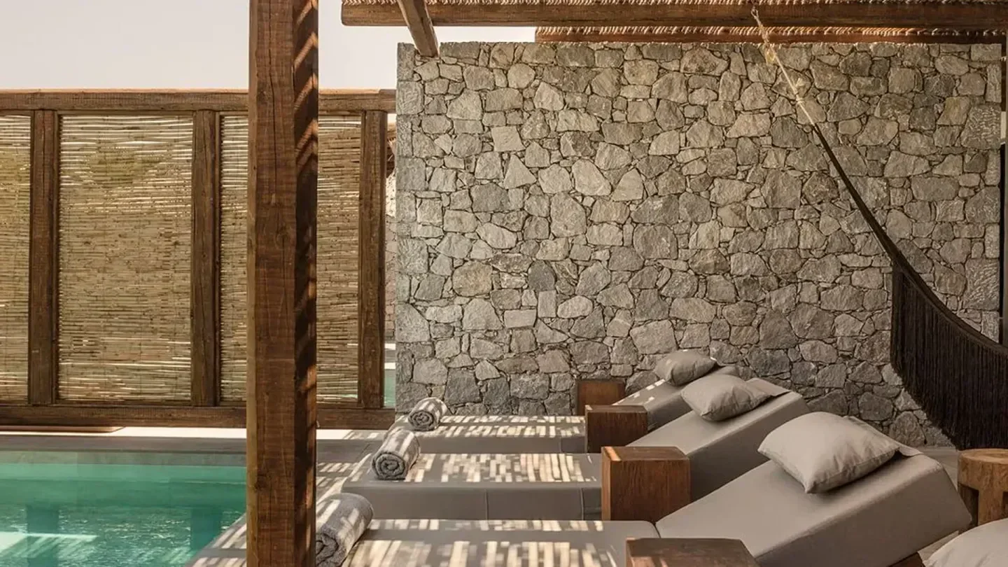 Relaxing sun loungers at OKU Ibiza beach club with stone wall and pool view.