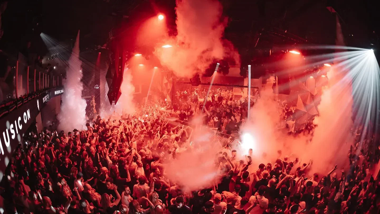 Energetic crowd partying at Pacha Ibiza nightclub, illuminated with red lights and smoke.
