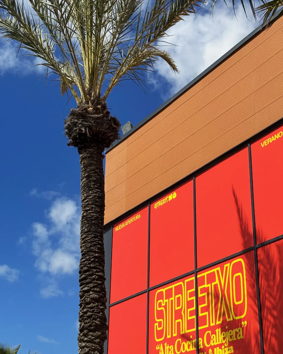 StreetXO Ibiza restaurant facade with bright red panels and a prominent palm tree against a blue sky.